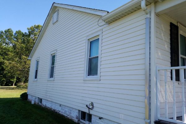 A white vinyl-sided home with clean windows and trim, set in a grassy yard, showcasing the results of gentle soft washing services ideal for property managers maintaining rental properties.