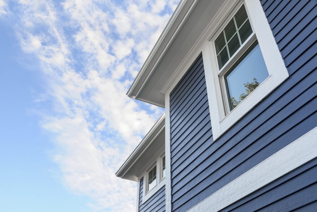 A close-up of a house with deep blue horizontal siding and crisp white trim under a bright blue sky, highlighting the clean, refreshed appearance after professional exterior cleaning in Ottawa Hills, OH.