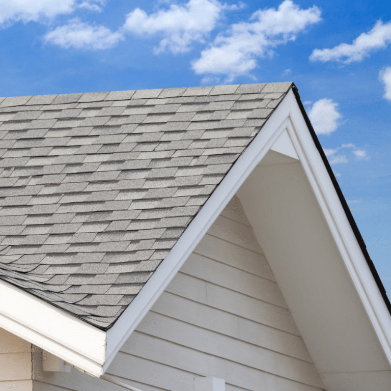 A clean, gray asphalt shingle roof with crisp white trim under a blue sky, showcasing the transformation achieved through professional roof cleaning services.