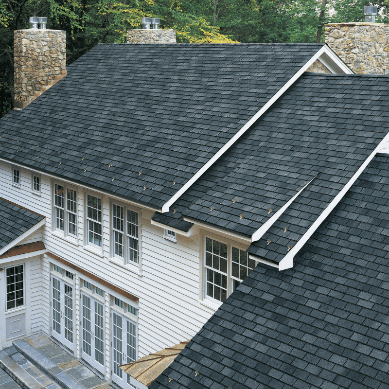 An aerial view of a clean, dark gray asphalt shingle roof on a white-sided home with stone chimneys, showcasing the results of expert roof cleaning in Ottawa Hills, OH.