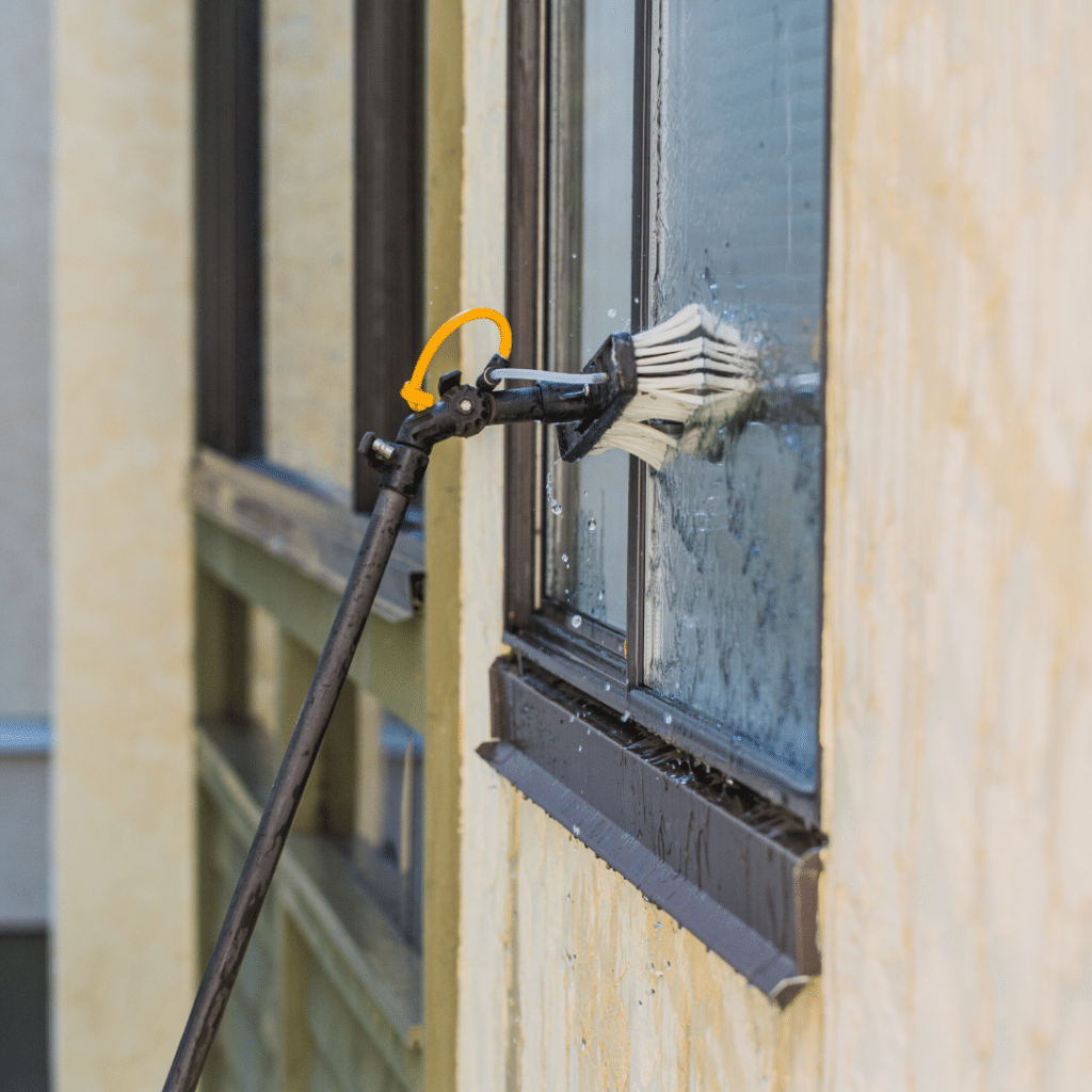 A water-fed pole with a brush attachment cleans a high-rise window, demonstrating a safe and effective method for professional window washing without ladders or scaffolding.