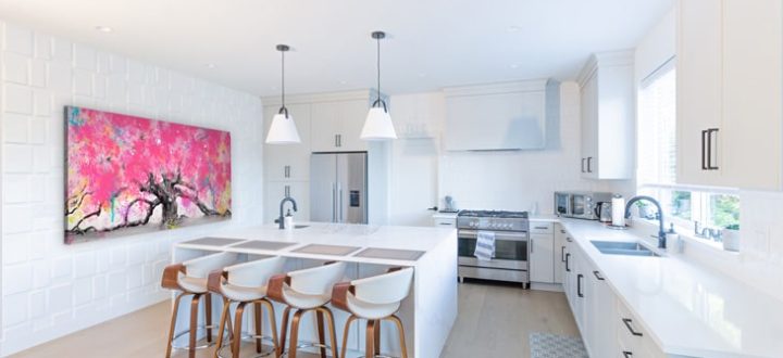 A bright, modern kitchen with white cabinetry, light wood flooring, and a large central island with bar stools. A vibrant pink abstract painting hangs on the wall, adding a pop of color. Stainless steel appliances and pendant lighting complete the sleek, contemporary design.